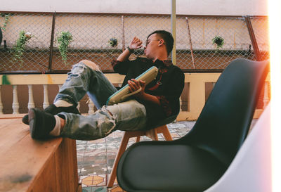 Full length of young man sitting on seat at building terrace