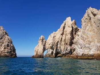 Rock formations in sea against clear blue sky