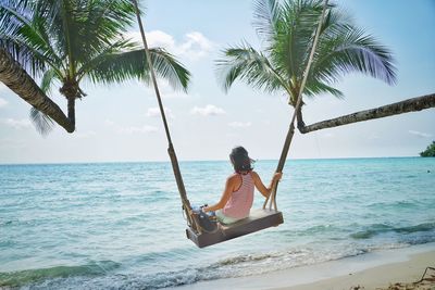 Man sitting on palm tree by sea against sky