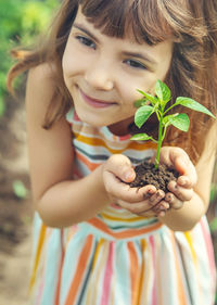 Cute girl holding plant while standing outdoors