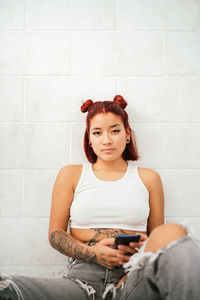 Portrait of a young woman using mobile phone against wall