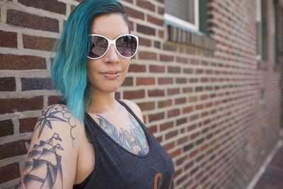 Portrait of young woman wearing sunglasses standing against brick wall