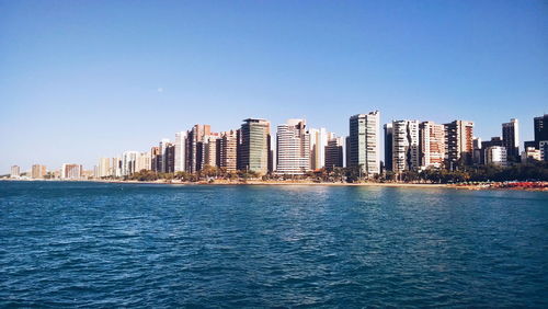 Sea in front of modern buildings against clear blue sky