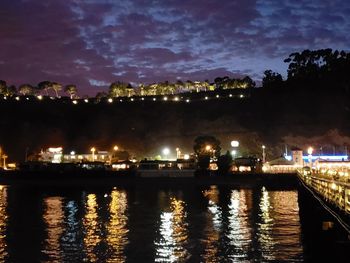 Illuminated buildings by river against sky at night