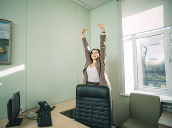 Smiling young caucasian female manager standing near chair stretching her arms. work-life-balance