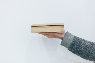 Close-up of hand holding book against white background