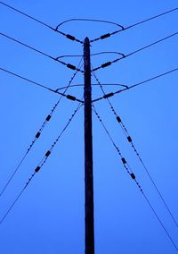 Low angle view of electricity pylon against clear blue sky