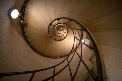 Top view of aged curved staircase with railing and lamps on rough wall in building
