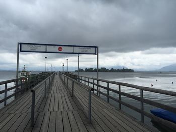 Road sign on pier by sea against sky