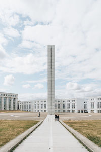 Walkway in city against cloudy sky