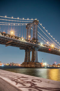 Illuminated bridge over river against sky in city at night