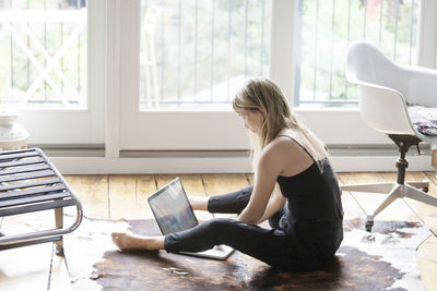 Woman using laptop while sitting on floor at home