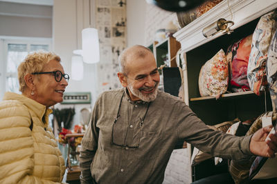 Happy senior owner assisting customer while buying cushions at home decor shop