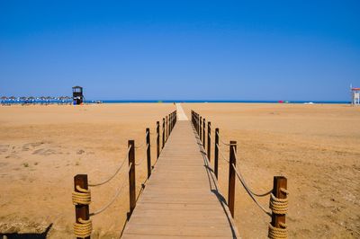 Wooden posts on beach against clear blue sky