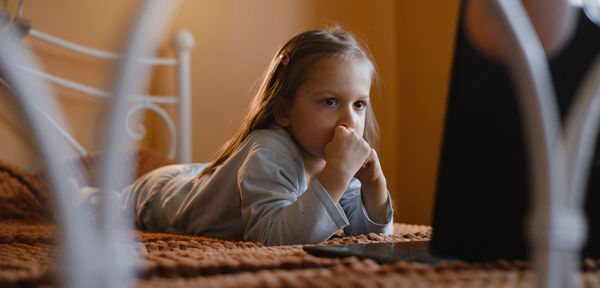 Child watching cartoons on laptop. serious kid with technology at home on bed spending time on-line