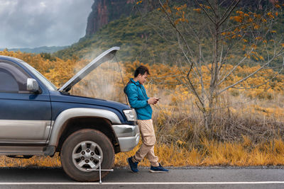 Side view of man using phone while standing by car on road