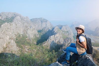 Man sitting on rock looking at mountains against sky