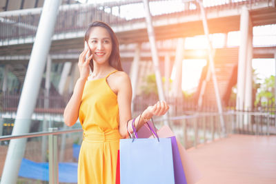 Happy young woman holding mobile phone while standing outdoors