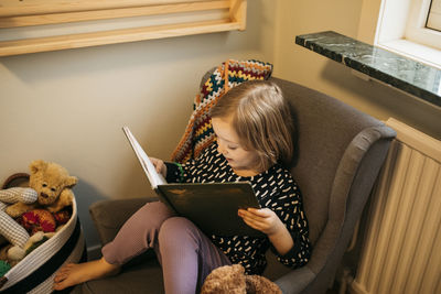 Girl sitting in armchair and reading book at home