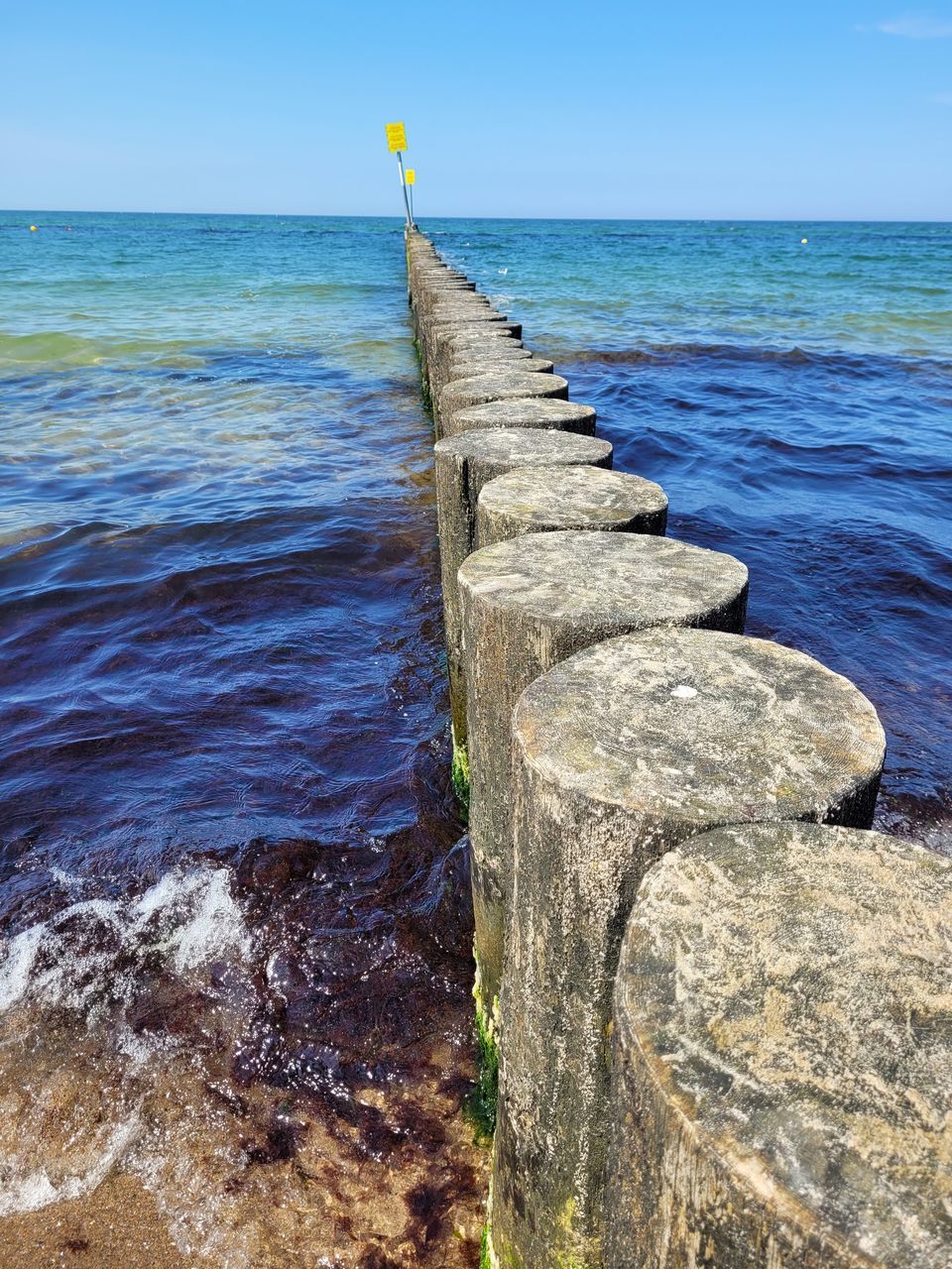 WOODEN POSTS ON ROCK AT SEA SHORE AGAINST SKY