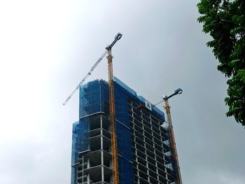 Low angle view of crane by building against sky