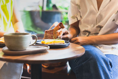 Woman eating lemom pie tart cake with coffee on table.