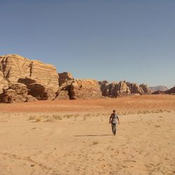 People on rock formations in desert against clear sky