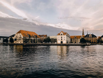 Buildings by river against sky in city