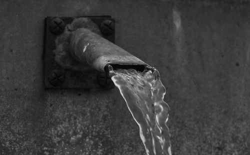 Close-up of water pouring from faucet against wall