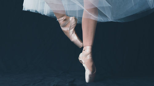 Low section of female ballet dancer dancing against black backdrop