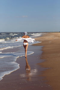 Woman run in a white bathing suit and hat sunglasses on an empty sandy beach