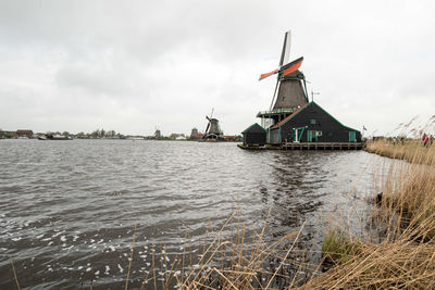 Traditional windmill by river against sky