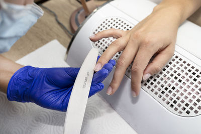 The manicurist shapes the nails with a nail file in blue latex gloves.