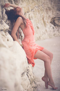 Young sensuous woman posing by rock at beach