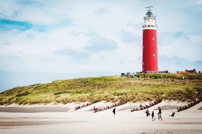People on beach by lighthouse against sky