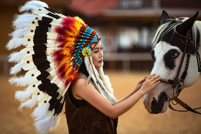 Close-up of woman wearing headdress while touching horse on field