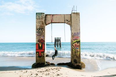 Man hanging with rope on structure at beach