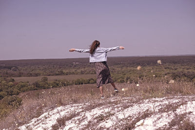 Woman with arms raised standing on field against sky