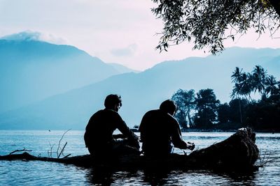 Silhouette people by lake against sky