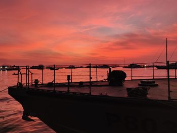 Silhouette boats moored in sea against orange sky