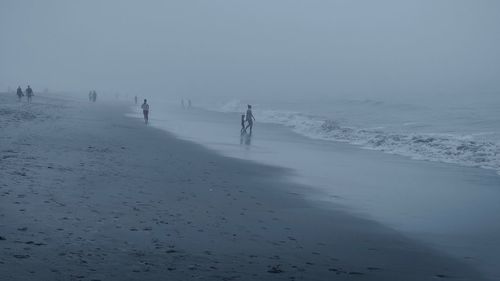 People at beach during fogy weather against sky