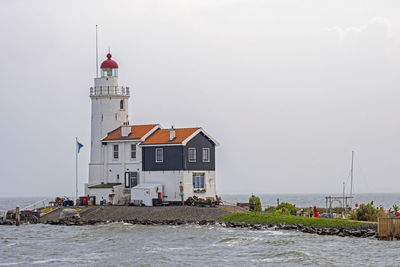 Lighthouse amidst sea and buildings against sky