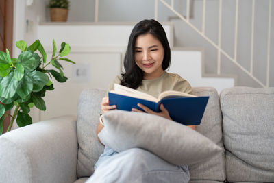 Young woman using phone while sitting on sofa at home