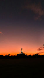 Silhouette statue on field against sky during sunset