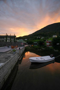 Boats moored on river by buildings against sky during sunset