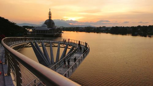 View of building by river against sky during sunset