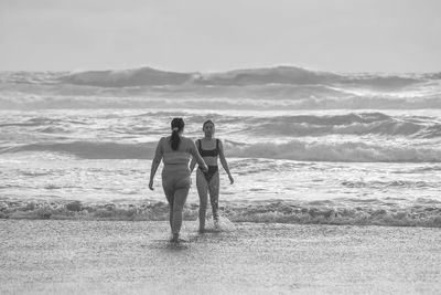 Rear view of men standing on beach against sky