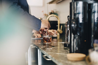 Midsection of businessman making tea while standing at kitchen counter in office