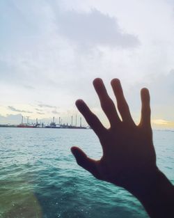 Close-up of hand on sea against sky