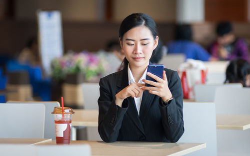 Young woman using phone while sitting on table